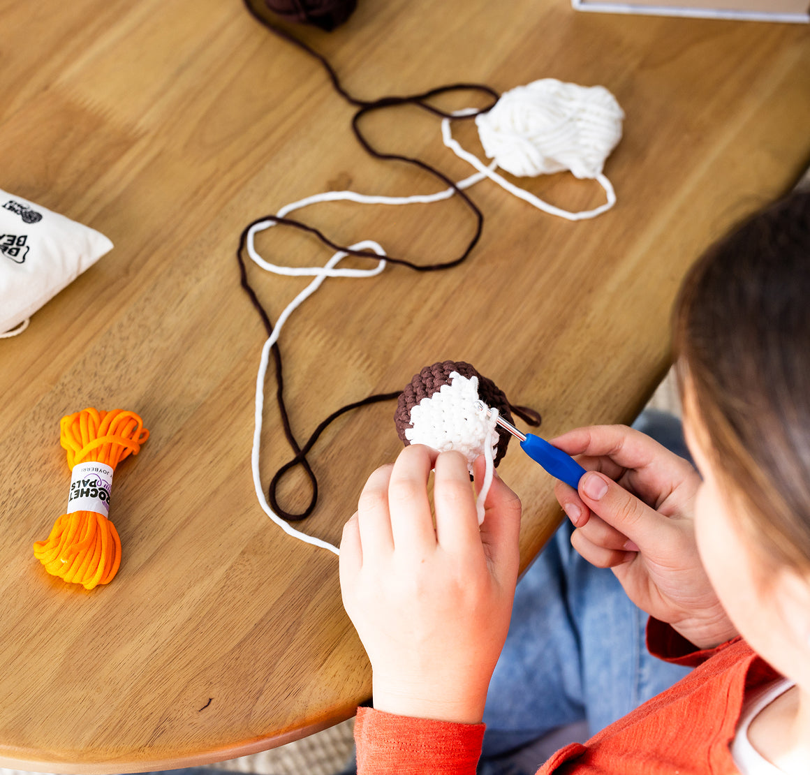 Person crocheting with yarn and a hook on a wooden table