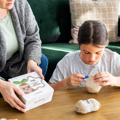 Woman and child sitting at a table with yarn and knitting materials