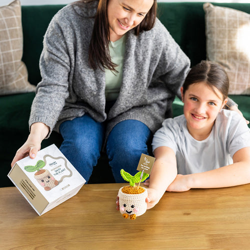 Woman and child sitting on a couch with a small potted plant and packaging on a table in front of them.