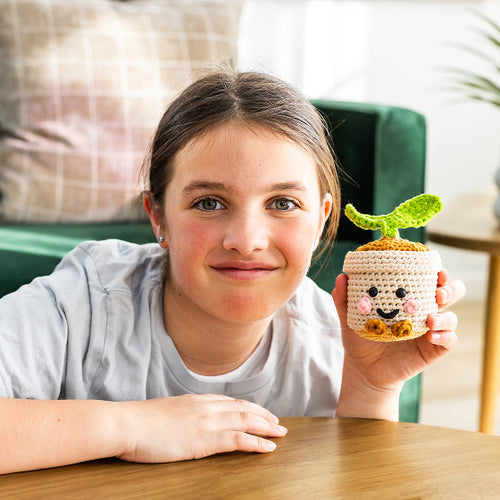 Young girl holding a small, crocheted plant pot with a face design.