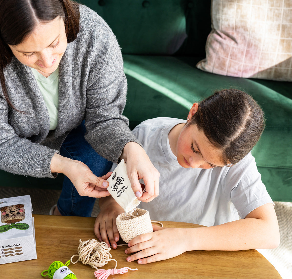 Woman and child sitting at a table with craft materials, possibly making a product.


