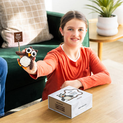 Child holding a plush owl toy next to a box on a table in a living room setting.
