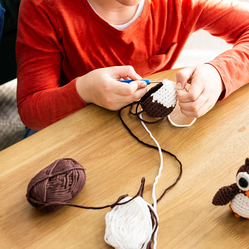 Person crocheting with yarn and a crochet hook on a wooden table.

