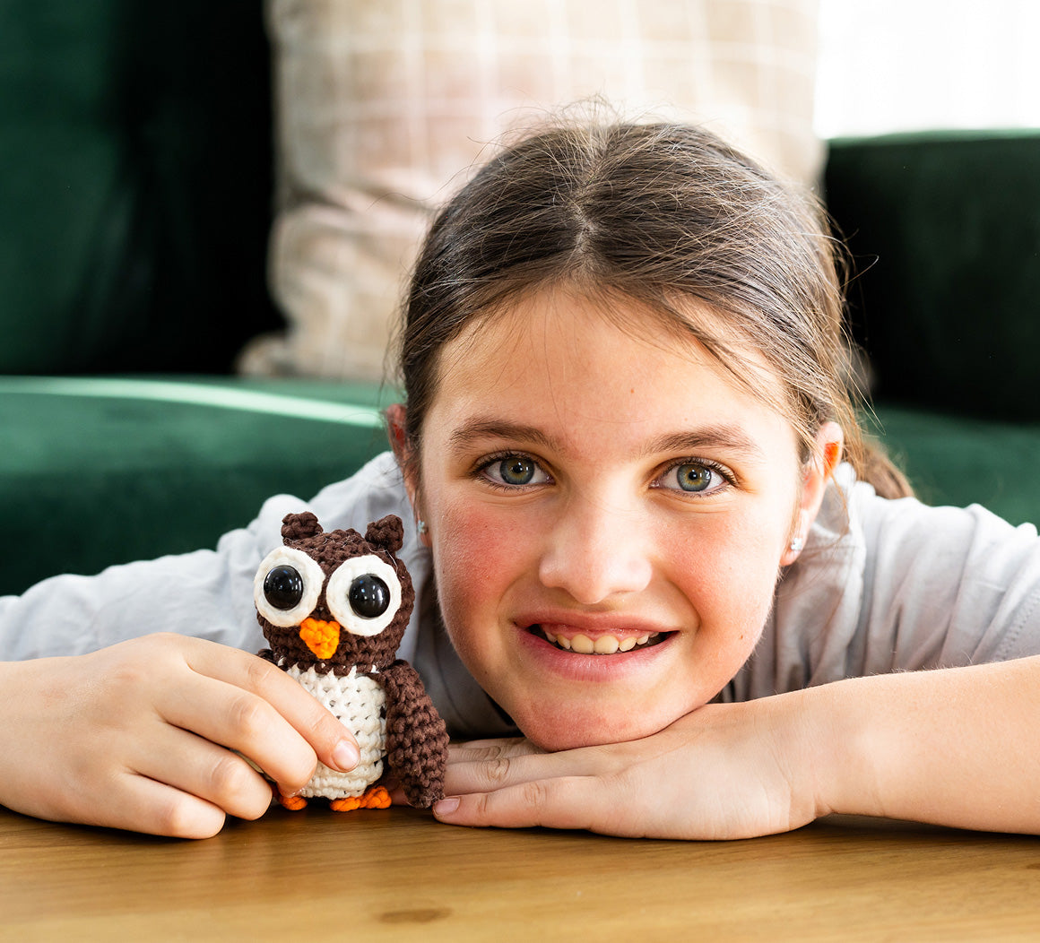 Young girl holding a crochet owl toy on a wooden table

