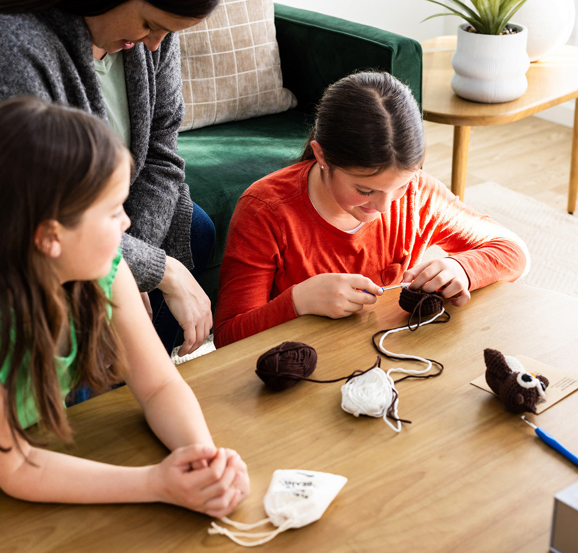 Two children and an adult sitting at a table making crafts in a cozy living room.
