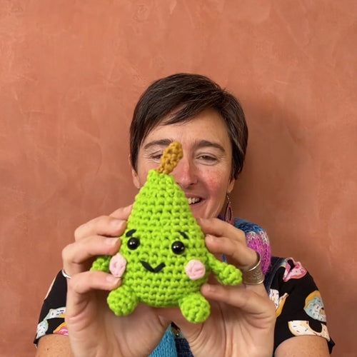 Person holding a green crochet toy against a brown background