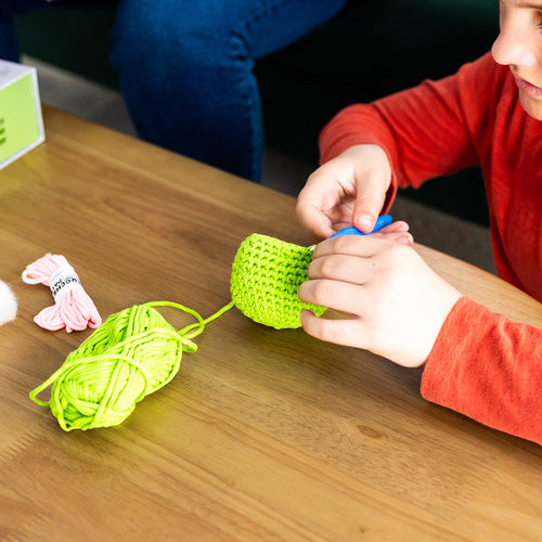 Child playing with a green crochet project on a wooden table