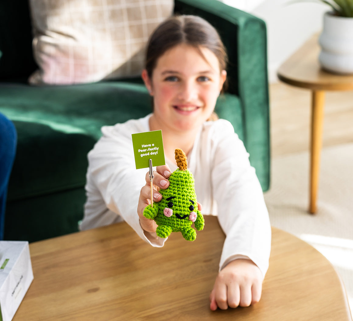  A girl is holding a green plush toy and a card with a smiley face, sitting on a couch.