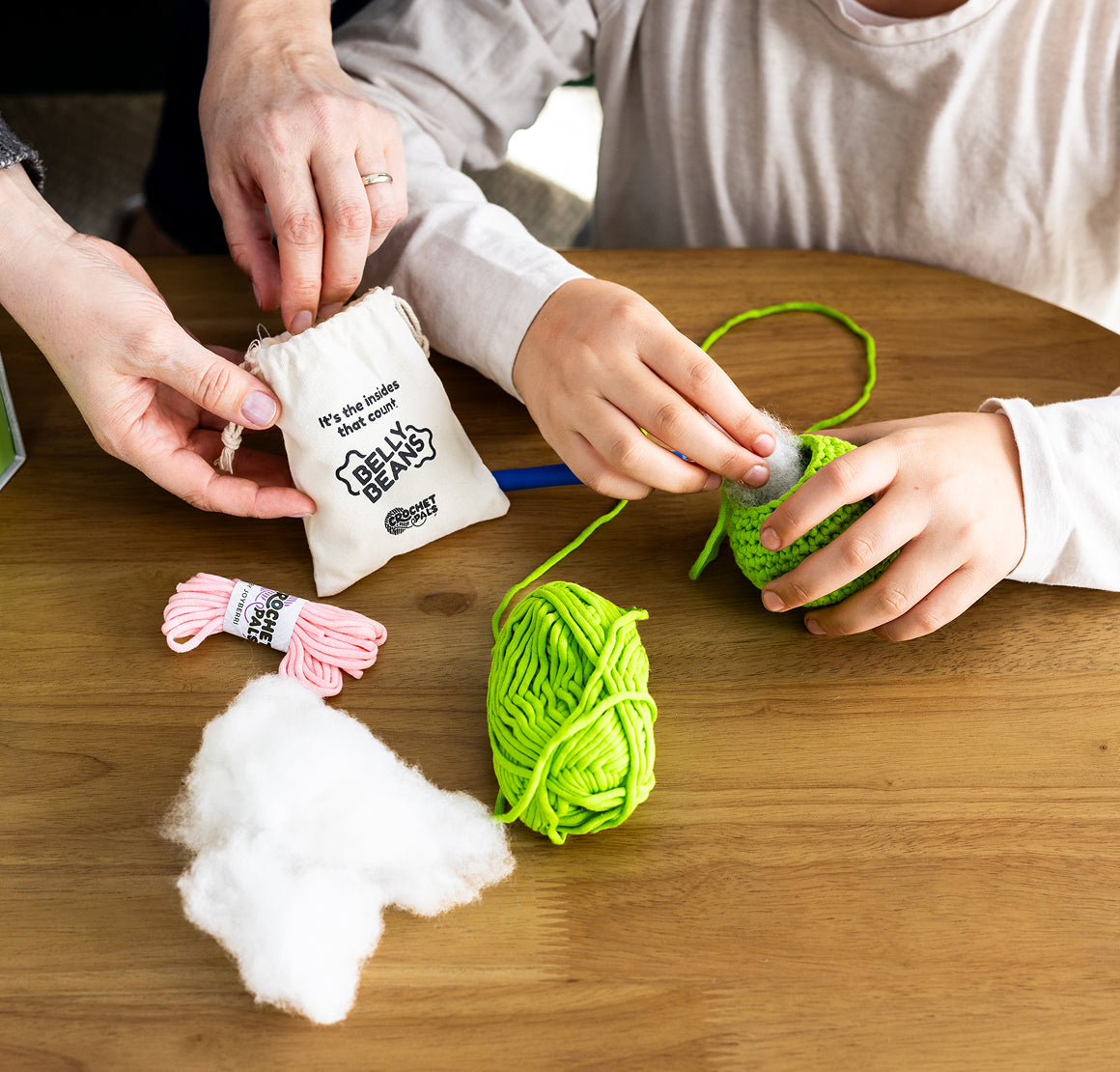 Two people working with yarn and a small bag on a wooden table.