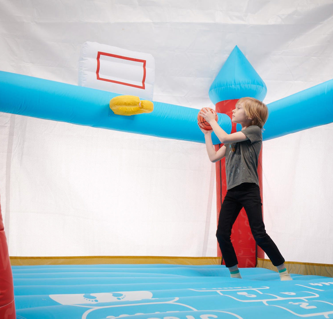 Child playing with an inflatable basketball hoop in a bouncy castle.