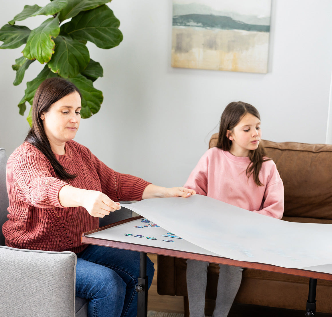 Woman and young girl sitting at a table with a large piece of paper, possibly working on a craft or art project.