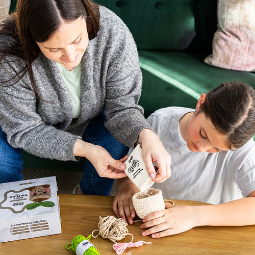 Two people working on a craft project with yarn  on a wooden table.