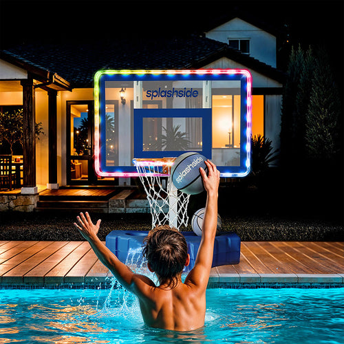 Person playing basketball in a pool with a 'Splashside' hoop at night.